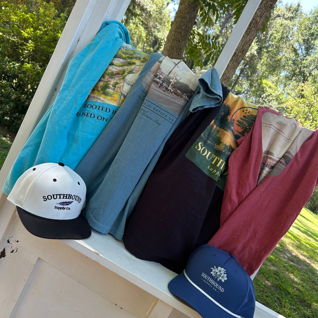 Clothing and accessories hanging on a white railing outdoors with trees in the background