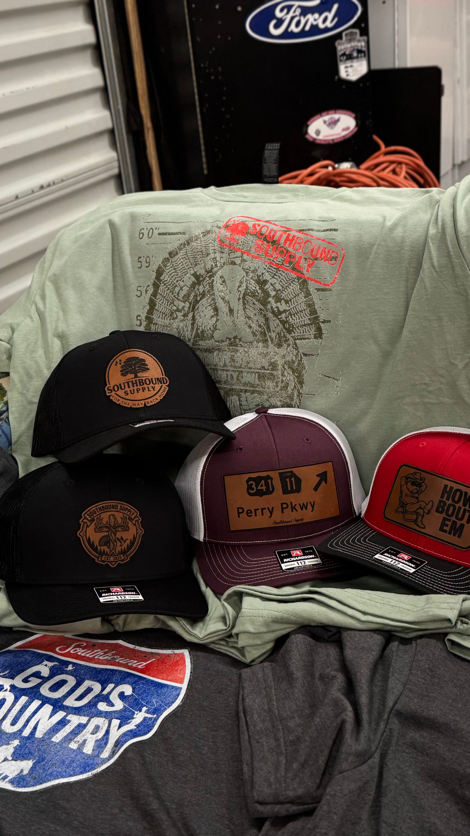 Three caps with embroidered designs on a green shirt with 'God's Country' text.